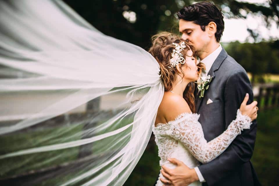 Best wedding photography capturing a romantic bride and groom kissing under a veil in a dreamy field.