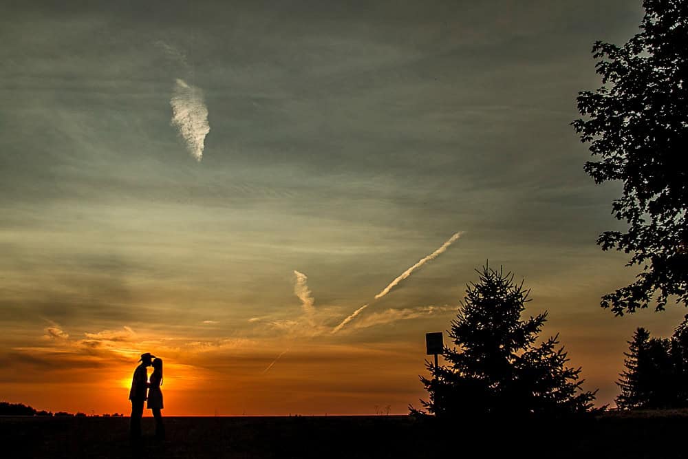 A beautiful silhouette of a couple kissing in front of a sunset captured in wedding photos.