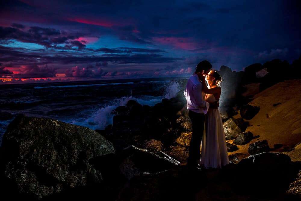 A stunning couple posing on rocks during a picturesque sunset for their wedding photos.