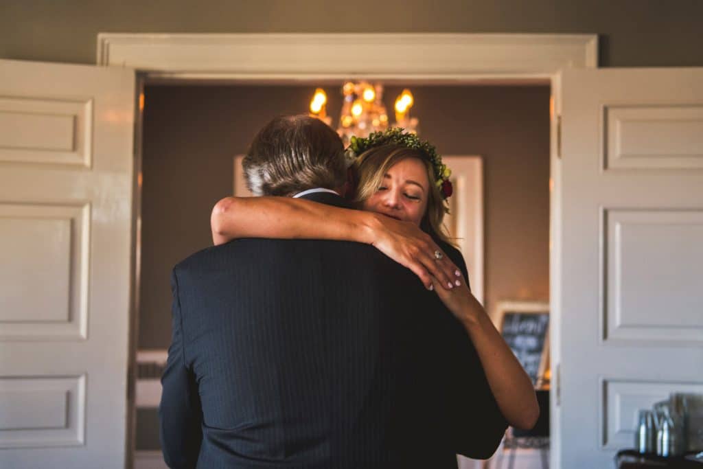Littleton Colorado Wedding Photographer A Littleton Wedding Photographer captures a bride hugging her father in front of a door.