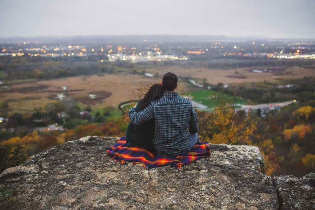 Hiking Engagement Photos A couple sitting on top of a mountain overlooking a city.
