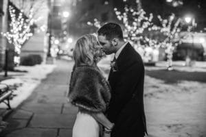 A bride and groom exchange a kiss amidst the enchanting glow of Christmas lights.