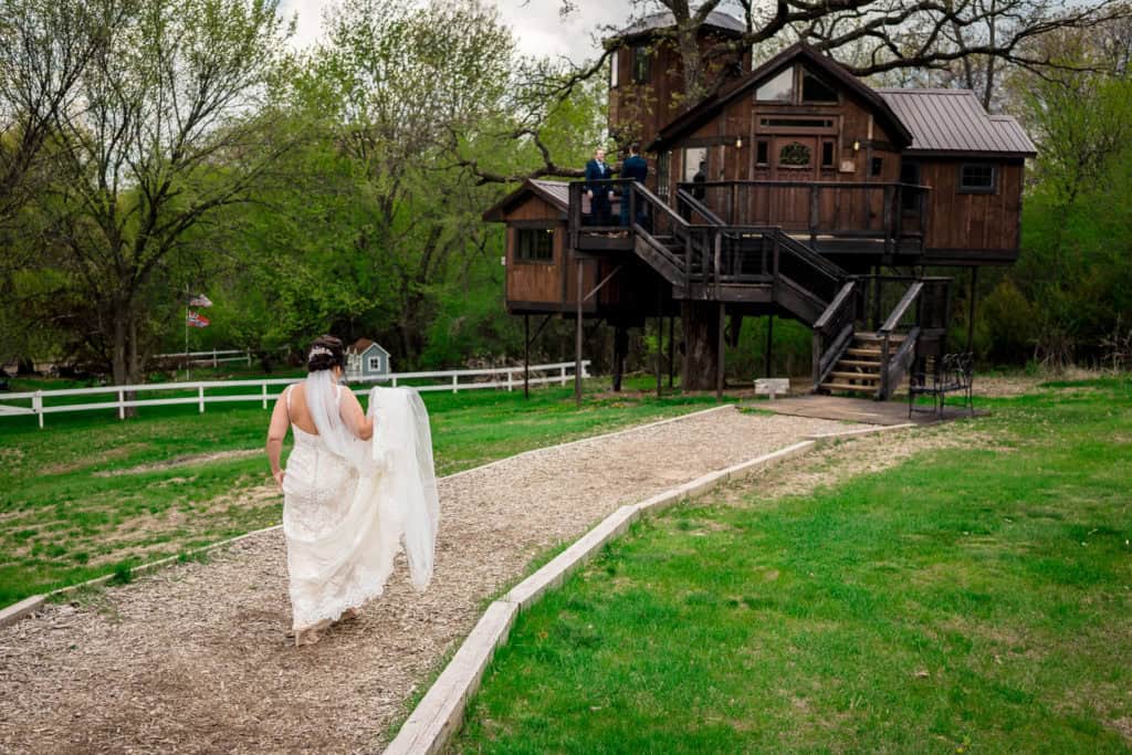 A bride walks down a path to a tree house.