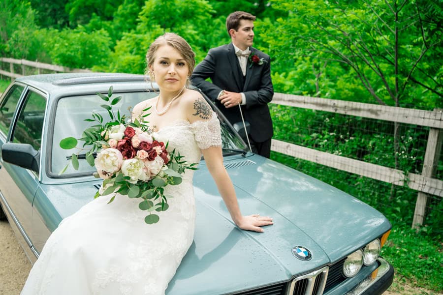 A bride and groom posing next to a blue bmw car.