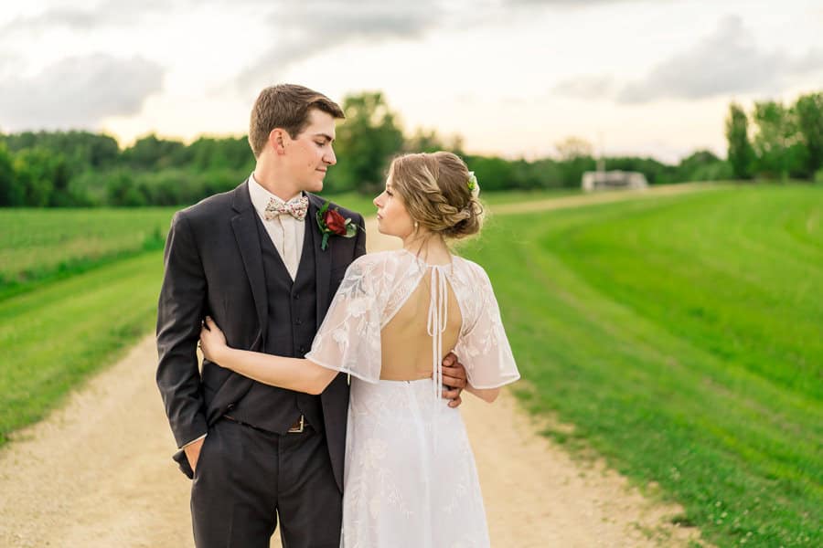 A bride and groom standing on a dirt road.