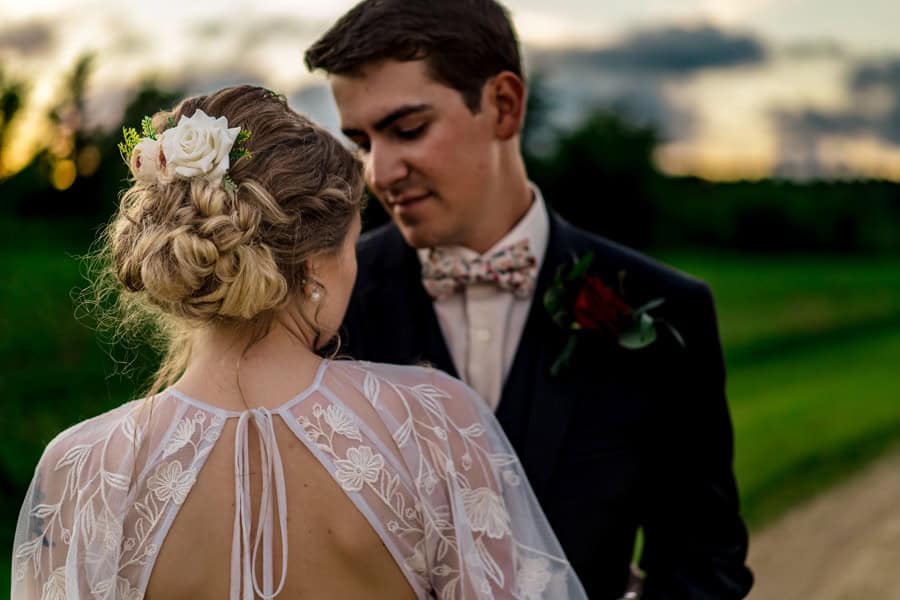 A bride and groom standing on a dirt road at sunset.