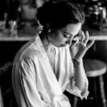 A woman in a robe is sitting in front of a mirror at Courtney and James' love-filled backyard Trempleau wedding.