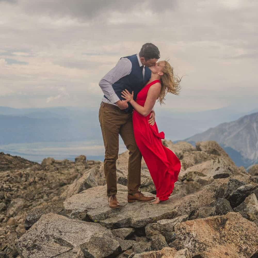 14er Engagement An engaged couple kissing on top of a mountain.