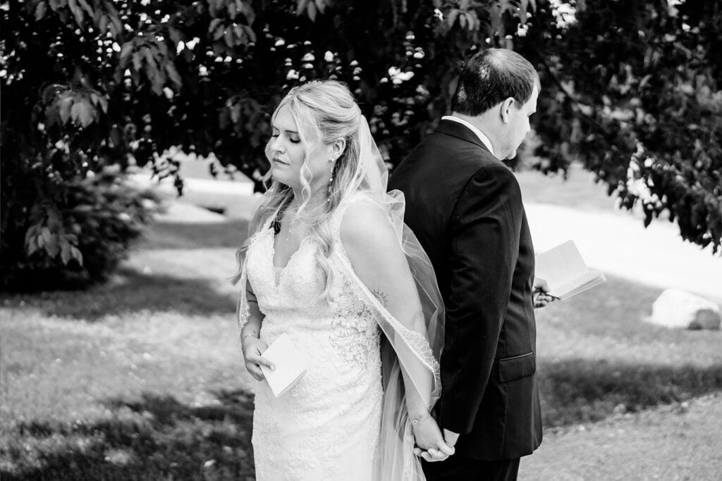 black-and-white-bride-groom-first-touch-vows-west-salem-wedding.jpg Bride and groom stand back to back outdoors during wedding ceremony at Maple Grove Events.