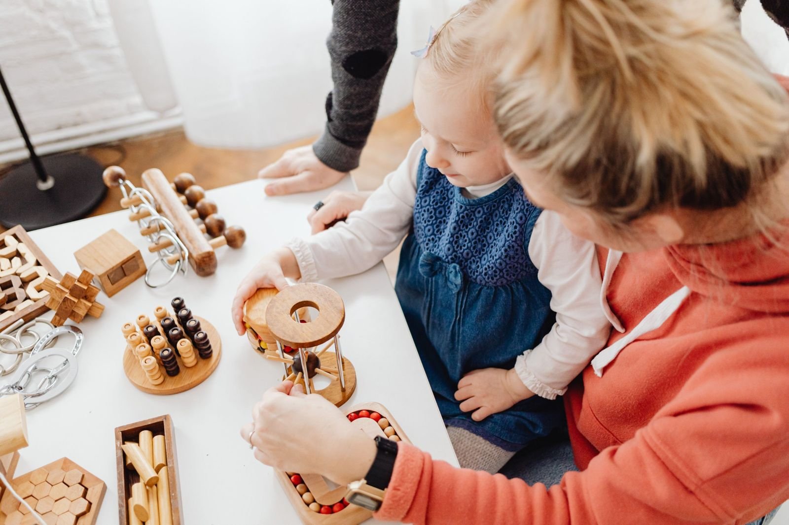 Caregiver and toddler exploring wooden puzzle toys together at a table
