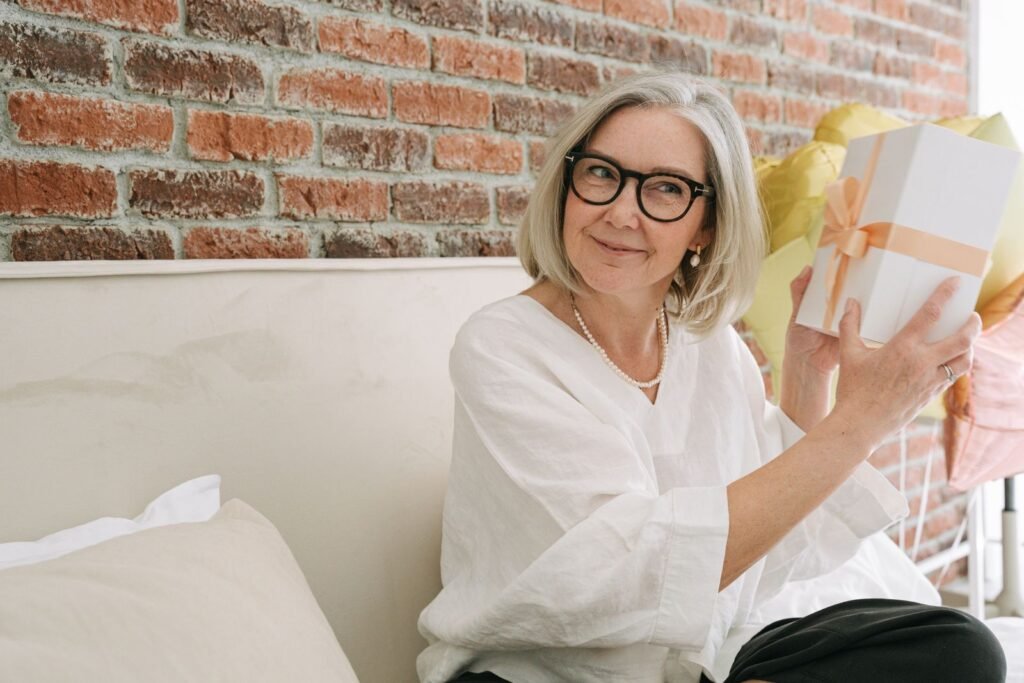 Smiling older woman in glasses holding a wrapped gift box at home