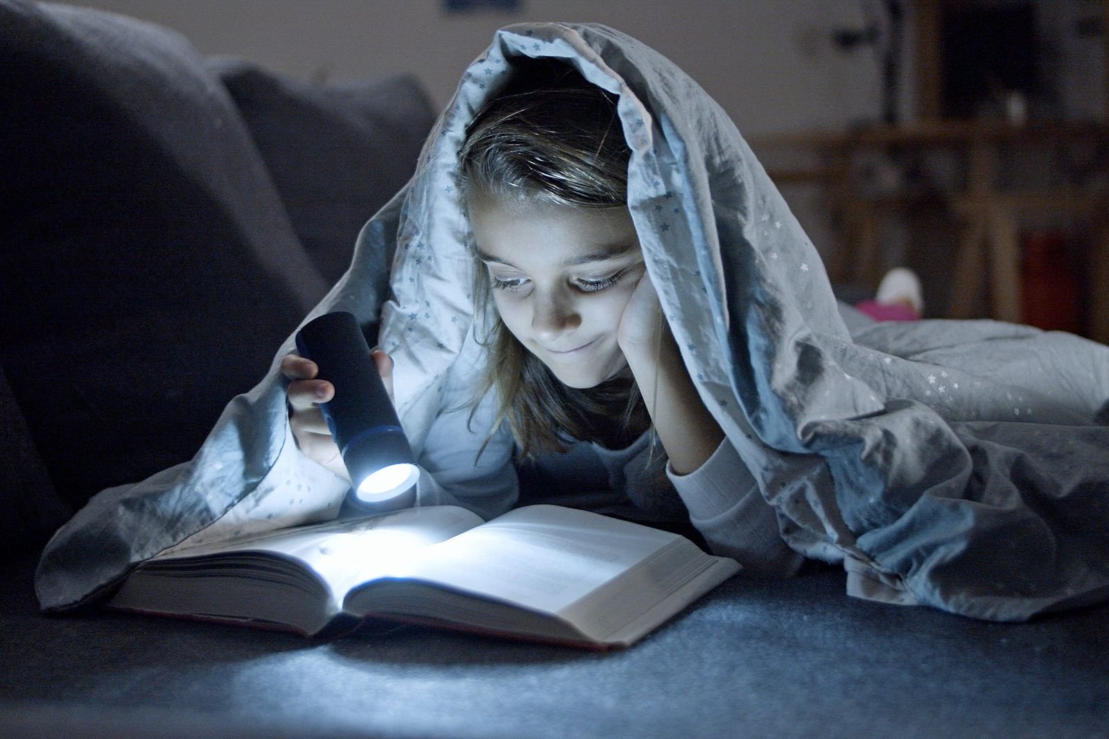 Girl reading a book under a starry blanket by soft flashlight glow