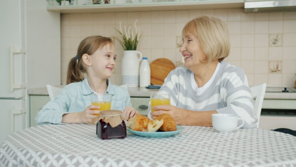 Grandmother and granddaughter smiling at each other over breakfast at the kitchen table
