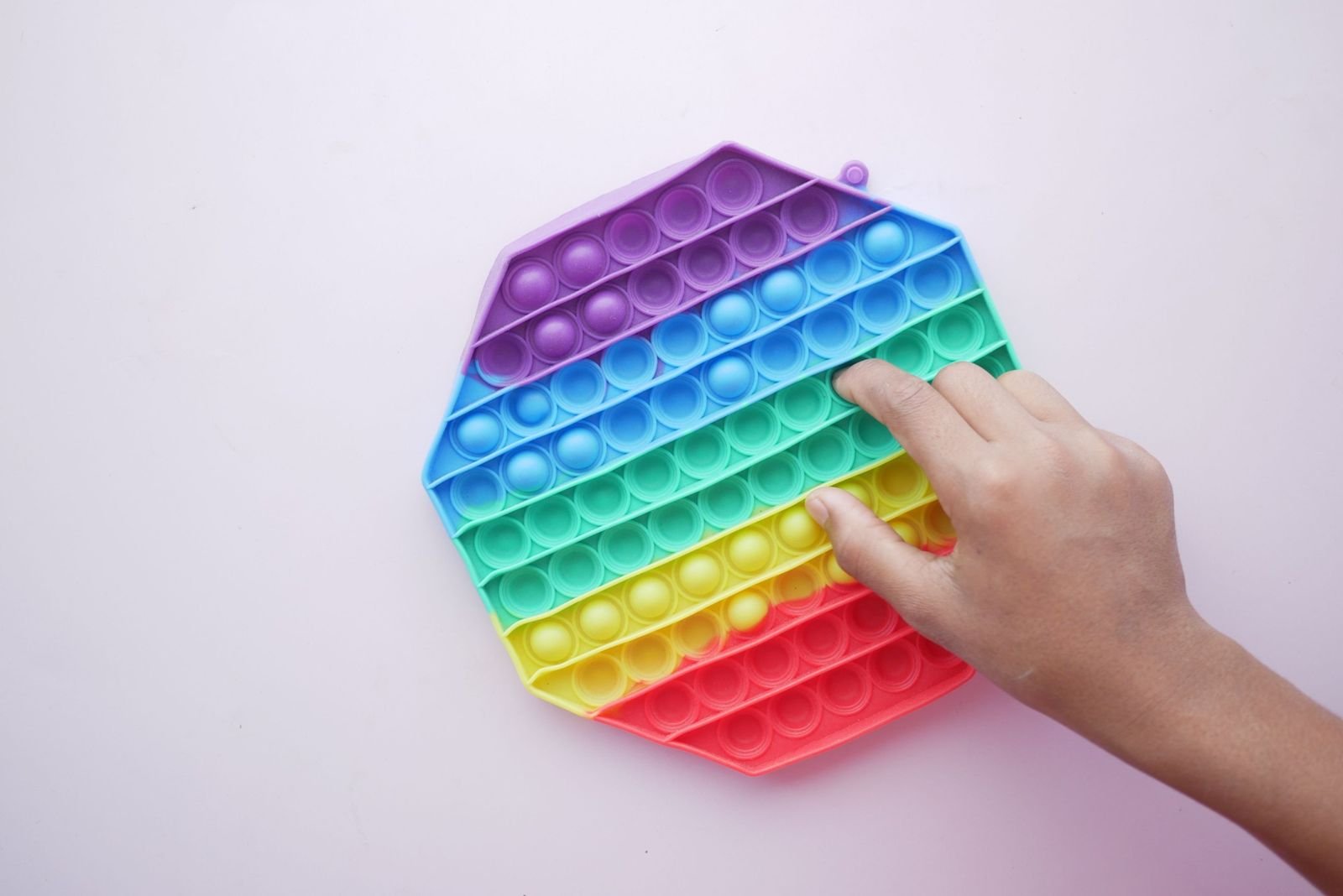 Hand pressing the bubbles of a rainbow octagon pop-it fidget toy