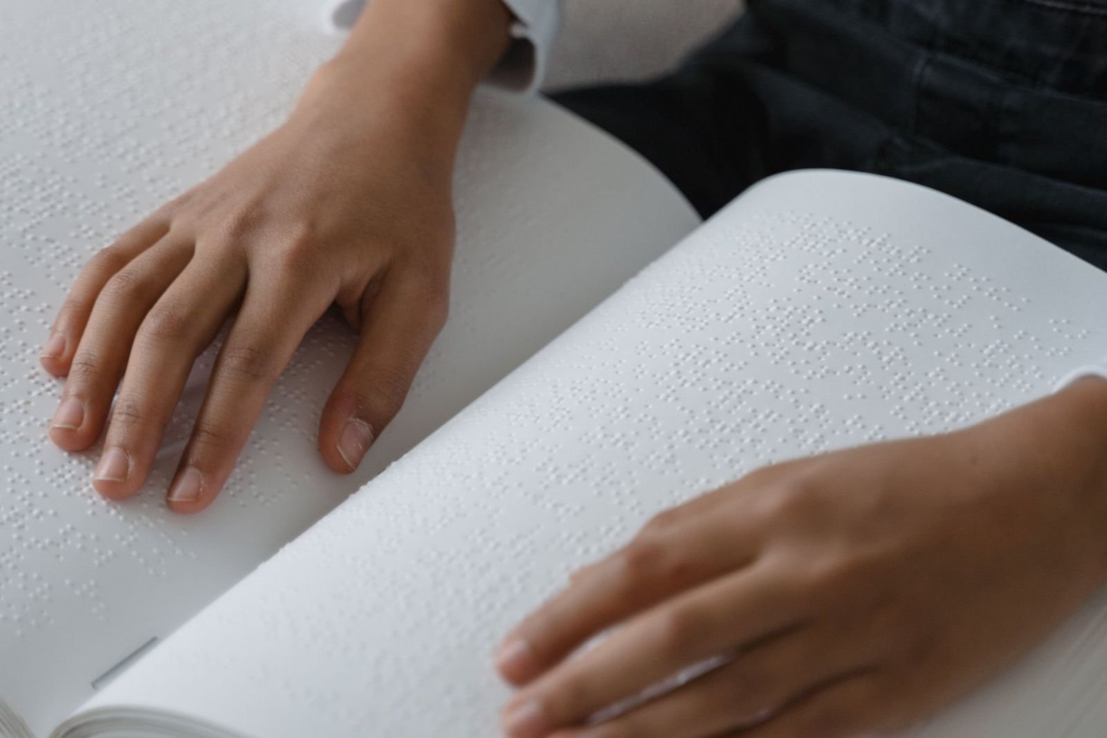 Hands reading the raised dots of an open braille book