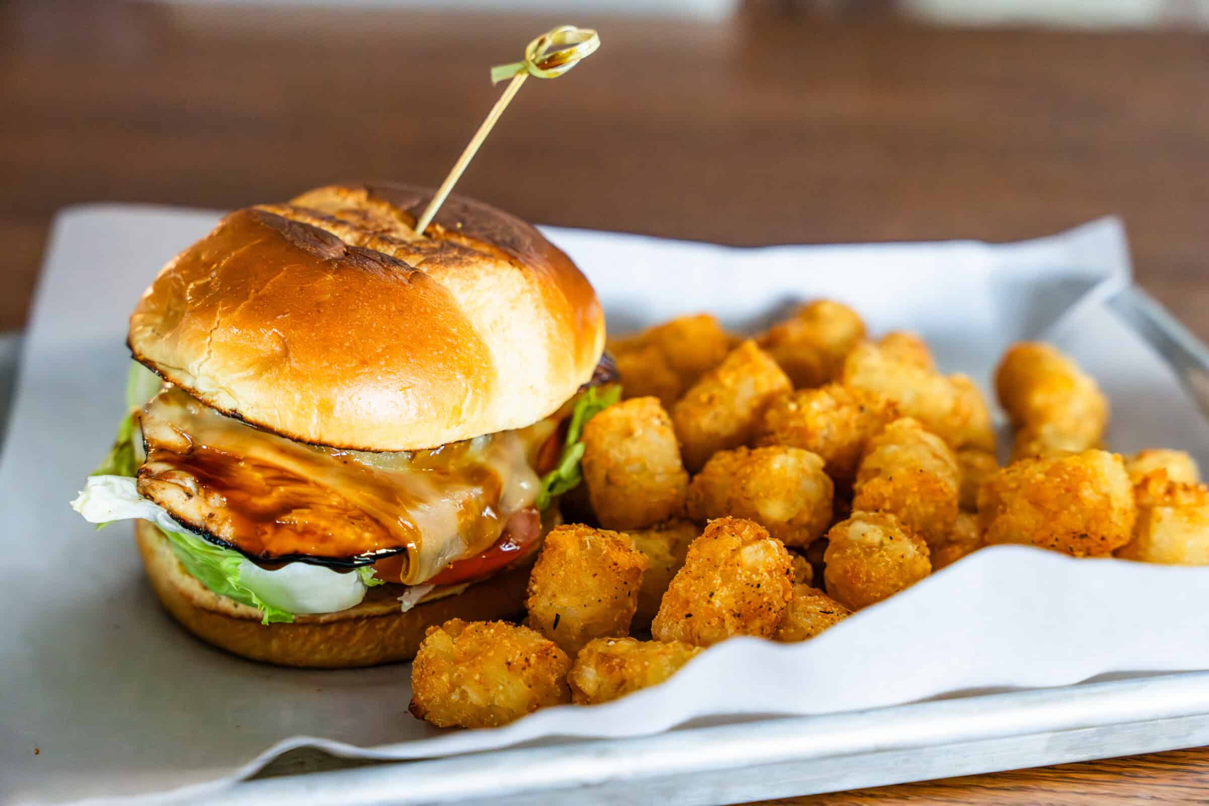 Hamburger with cheese and lettuce on a plate with tater tots.