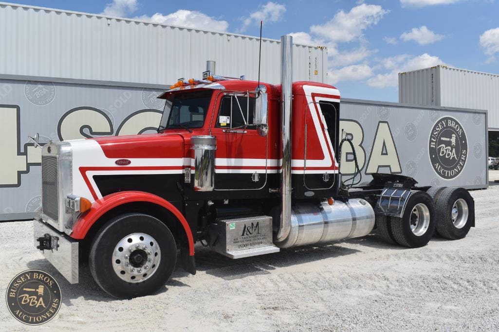 Semi-truck with red, black, and white paint, parked outdoors with shipping containers in the backgro.