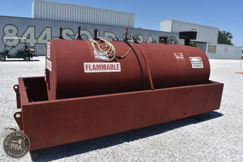 Large red flammable fuel storage tank with safety labels at auction site.