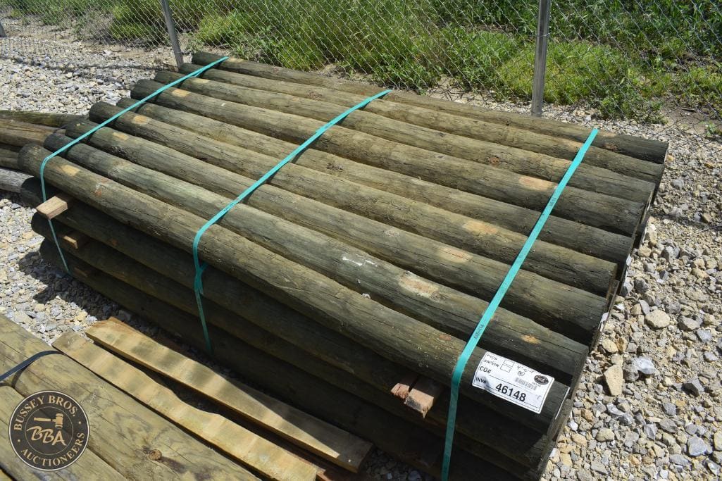 Bundle of weathered wooden fence posts stacked outdoors for sale.