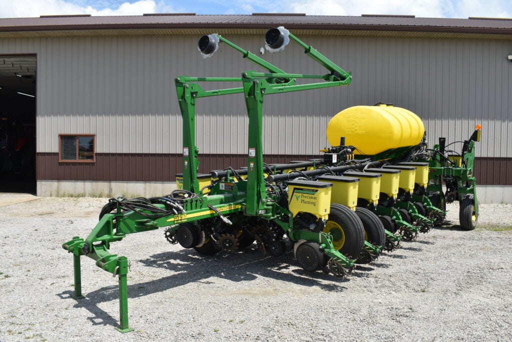 Green John Deere planter with yellow seed tank at auction site.