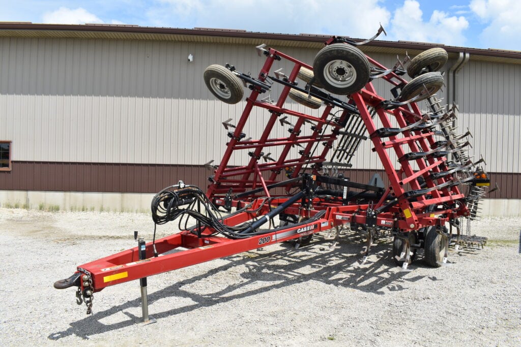 Red farm implement with multiple wheels and tines for agricultural use.
