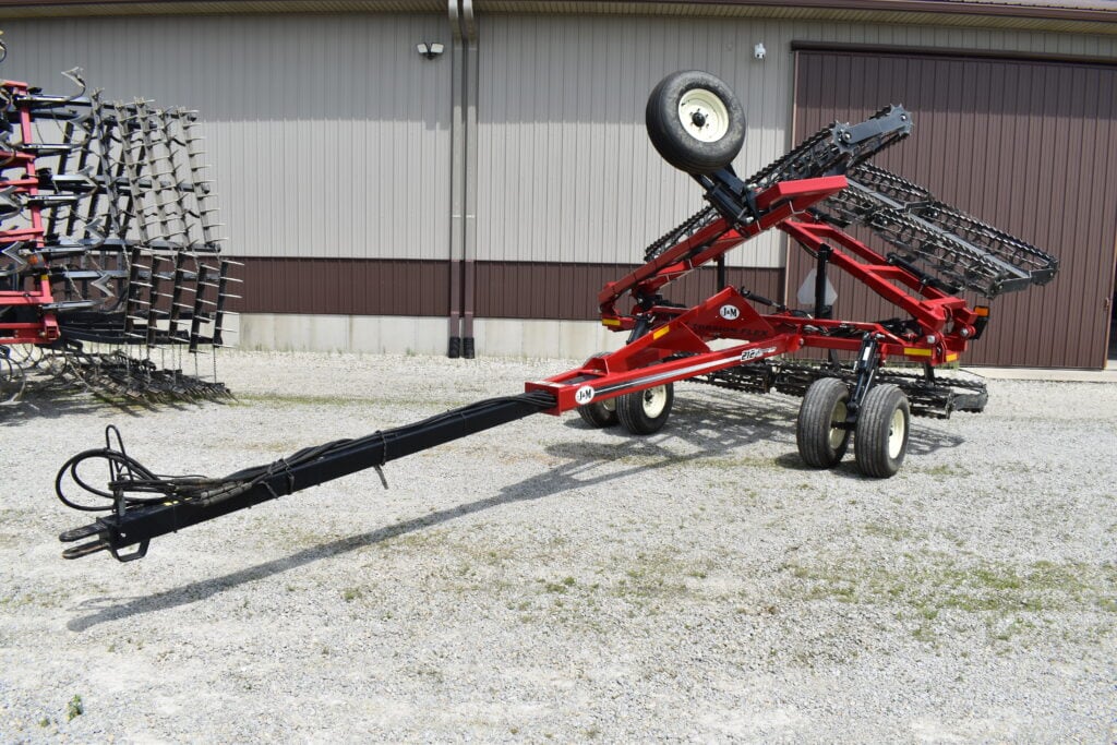 Red farm implement with wheels and tines for soil cultivation.