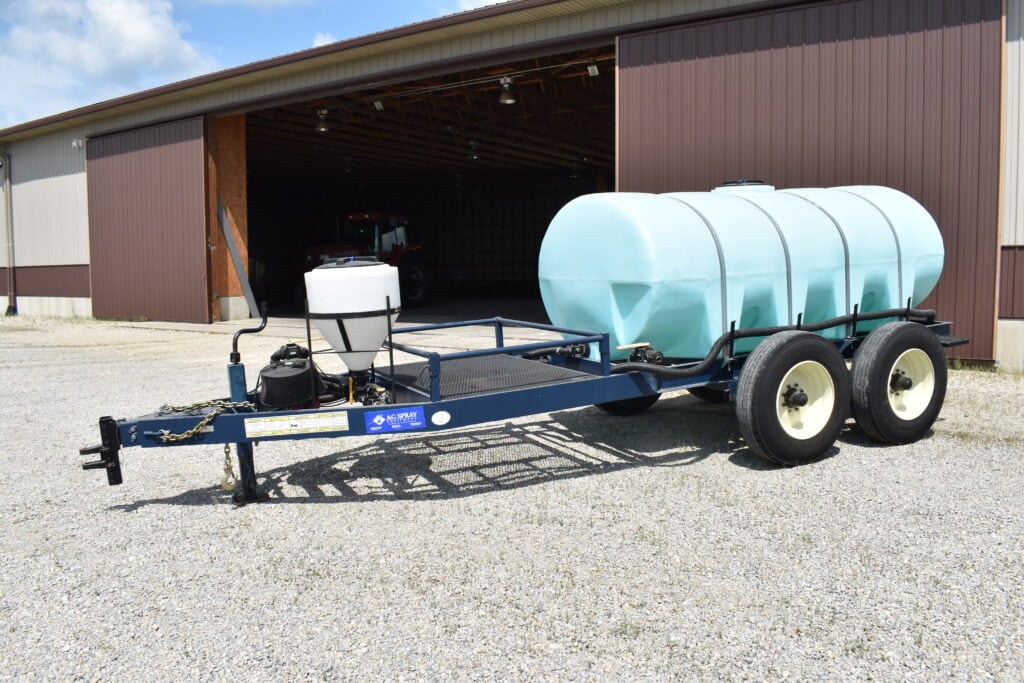 Farm water tank trailer with dual wheels and pump system outside barn.