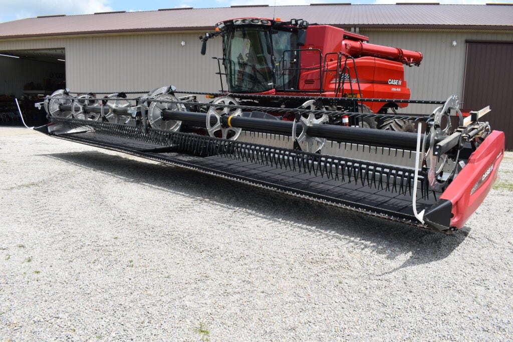 Red Case harvesting combine at auction with large cutting header.
