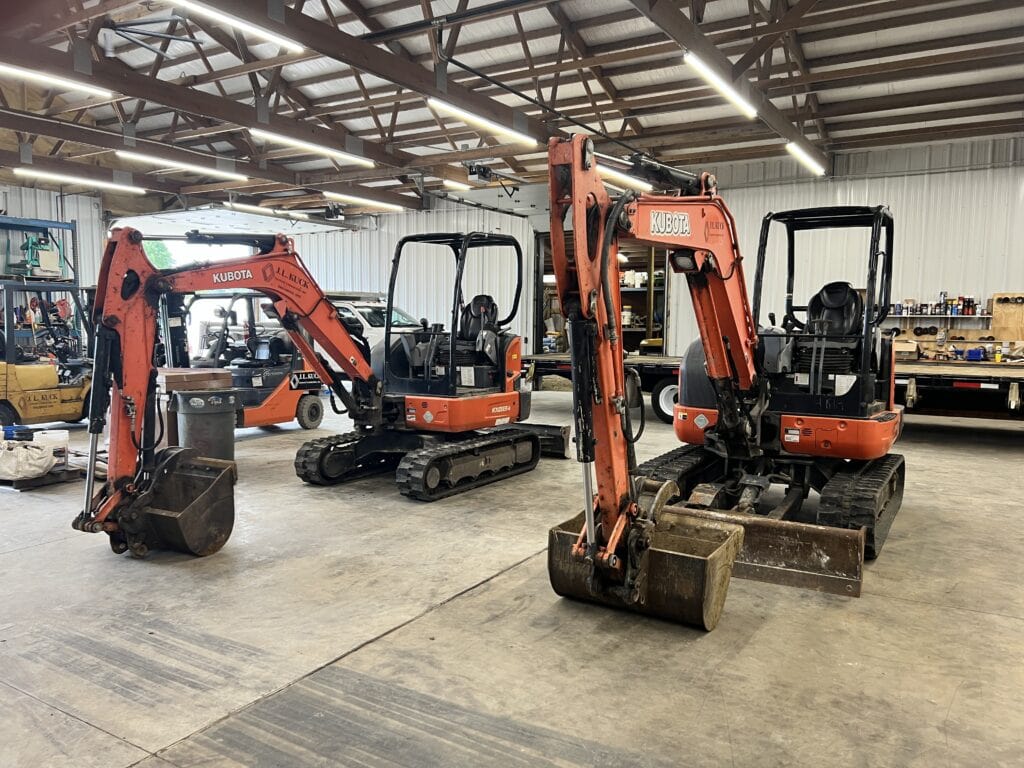 Three mini excavators inside a warehouse for auction.