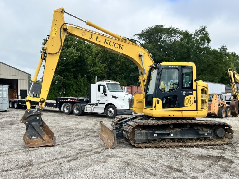 Yellow J.L. Kuck excavator at auction site with trucks and trees in background.