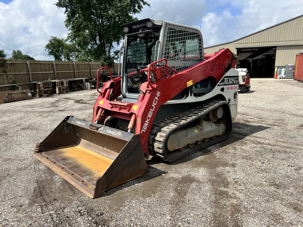 Red Takeuchi compact track loader with bucket attachment on gravel lot.