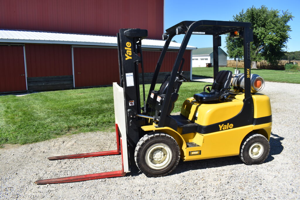 Yellow Yale forklift on gravel with red barn in background.