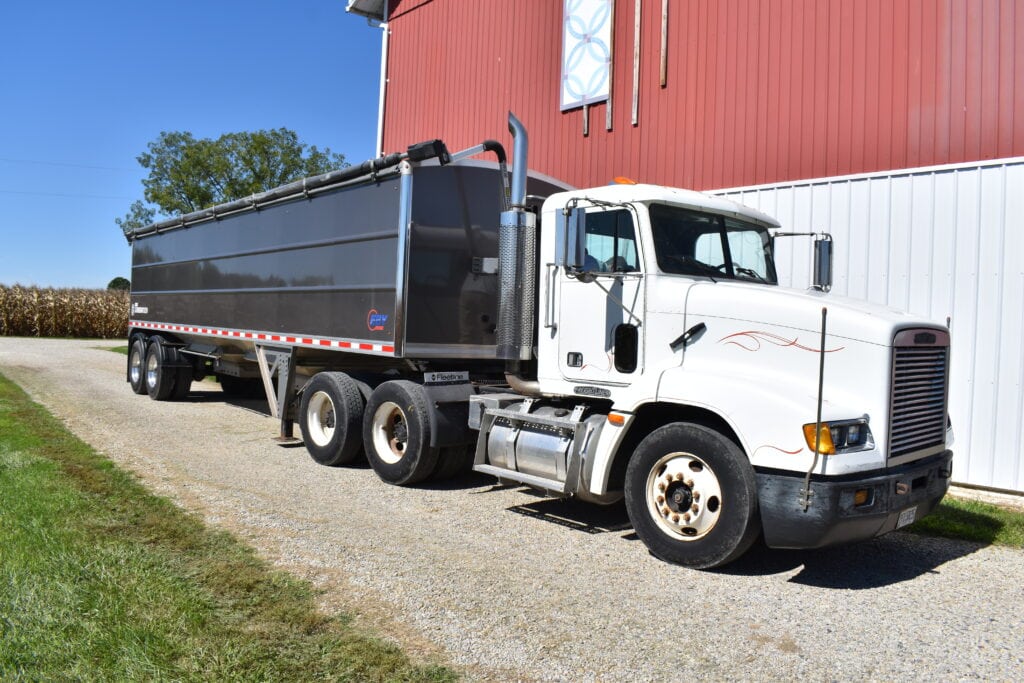 White and black dump truck parked outside red barn at auction.