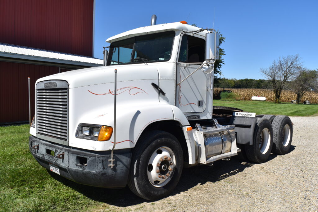 White Freightliner semi truck at auction site with clear sky.
