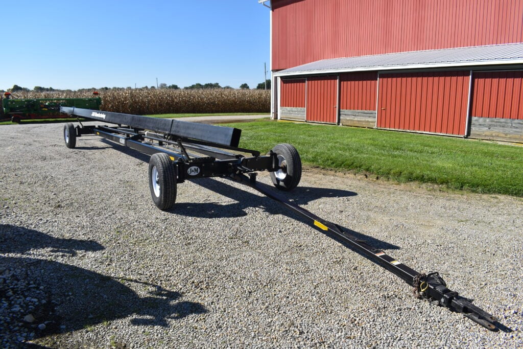 Farm equipment trailer on gravel with red barn in background.