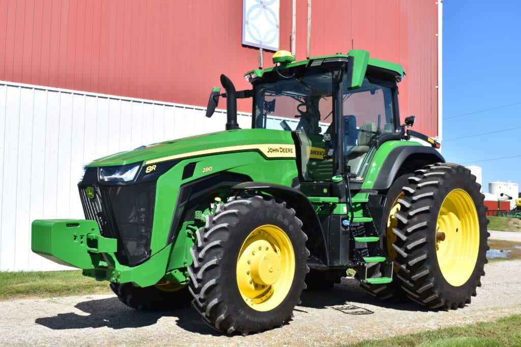 Green John Deere 8R tractor with large tires at auction site.