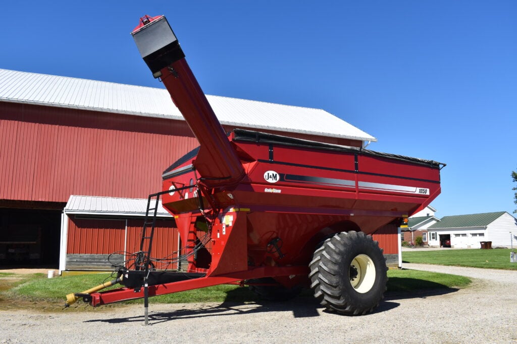 Large red grain cart with unloading auger at farm auction.
