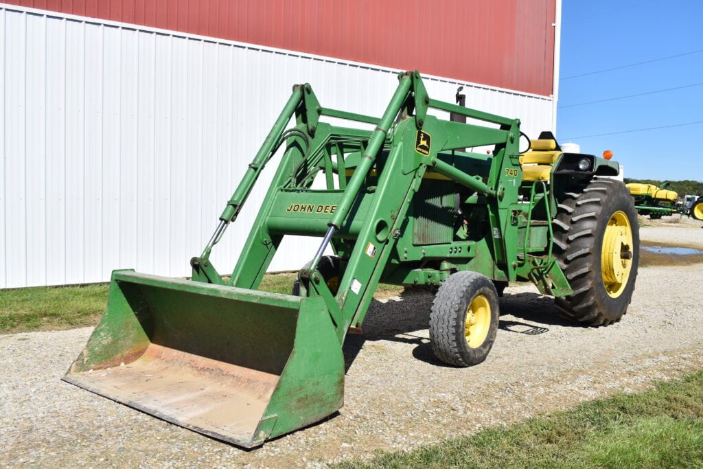Green John Deere tractor with front loader at auction site.