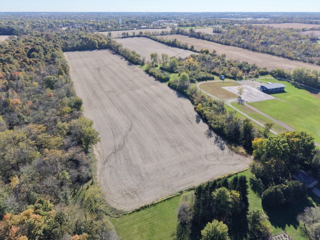 Aerial view of farmland with fields, trees, and a small building in a rural area.