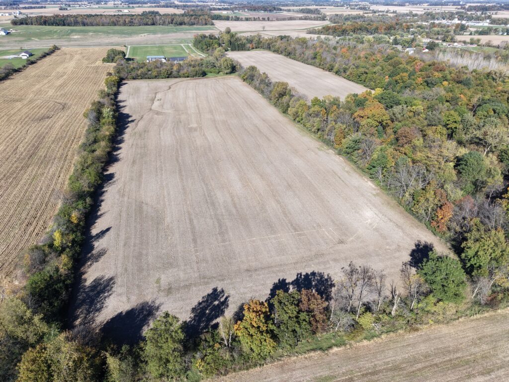 Aerial view of farmland with open fields and surrounding trees in a rural area.