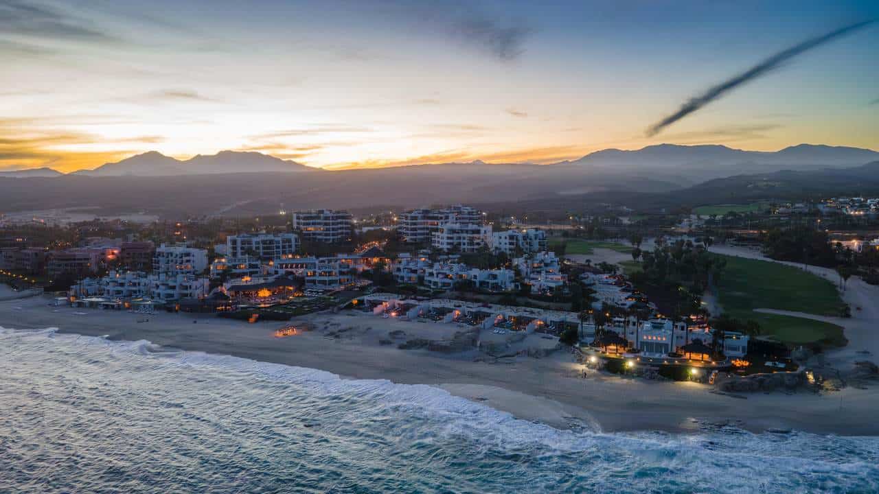 Stunning Aerial View Of Cabo Real Beachfront Resort At Sunset With Mountains In The Background, Highlighting Luxury Real Estate And Oceanfront Properties In Cabo Real.