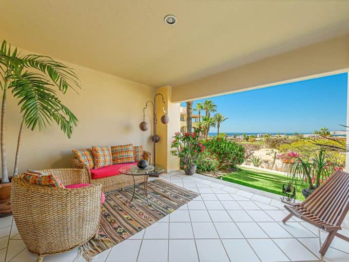 Vibrant Cabo Real Balcony With Lush Plants, Ocean View, Wicker Furniture, And Colorful Decor, Ideal For Relaxing In Cabo Real'S Luxurious Real Estate Properties.