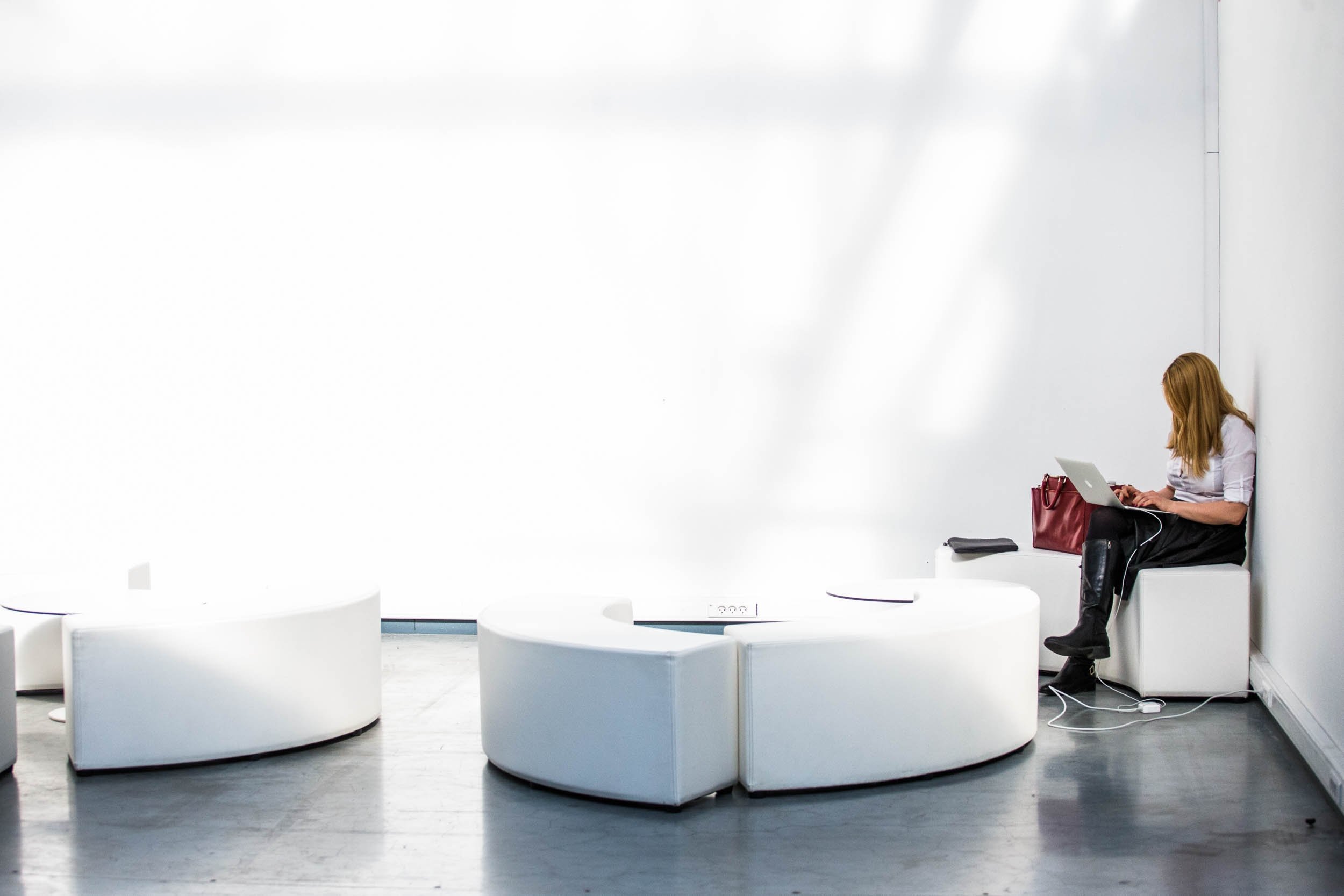 A photograph of a woman sitting in an empty lounge room working on her computer