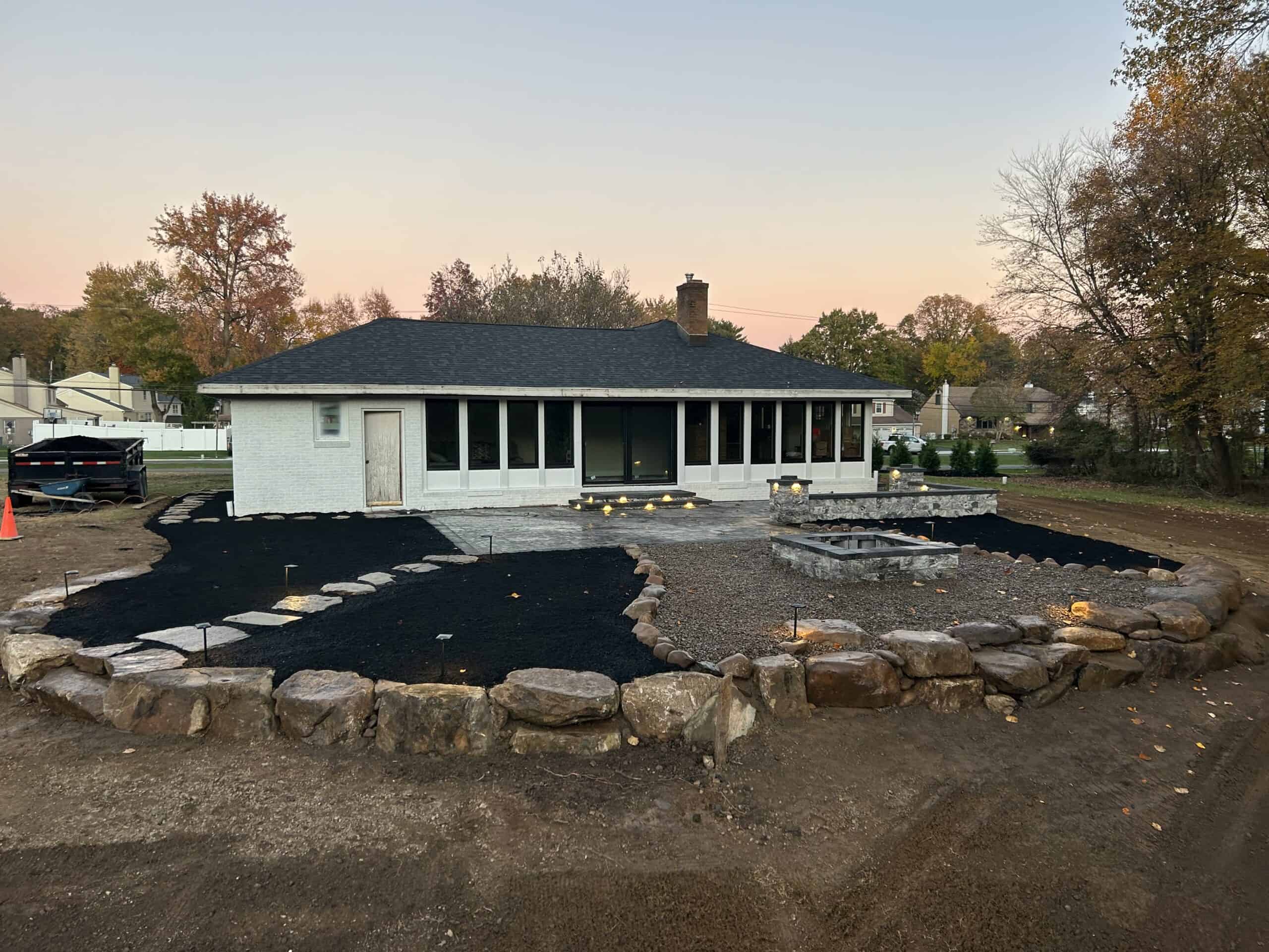 Backyard landscape design featuring a stone-bordered patio under construction by C&J Outdoor Service.