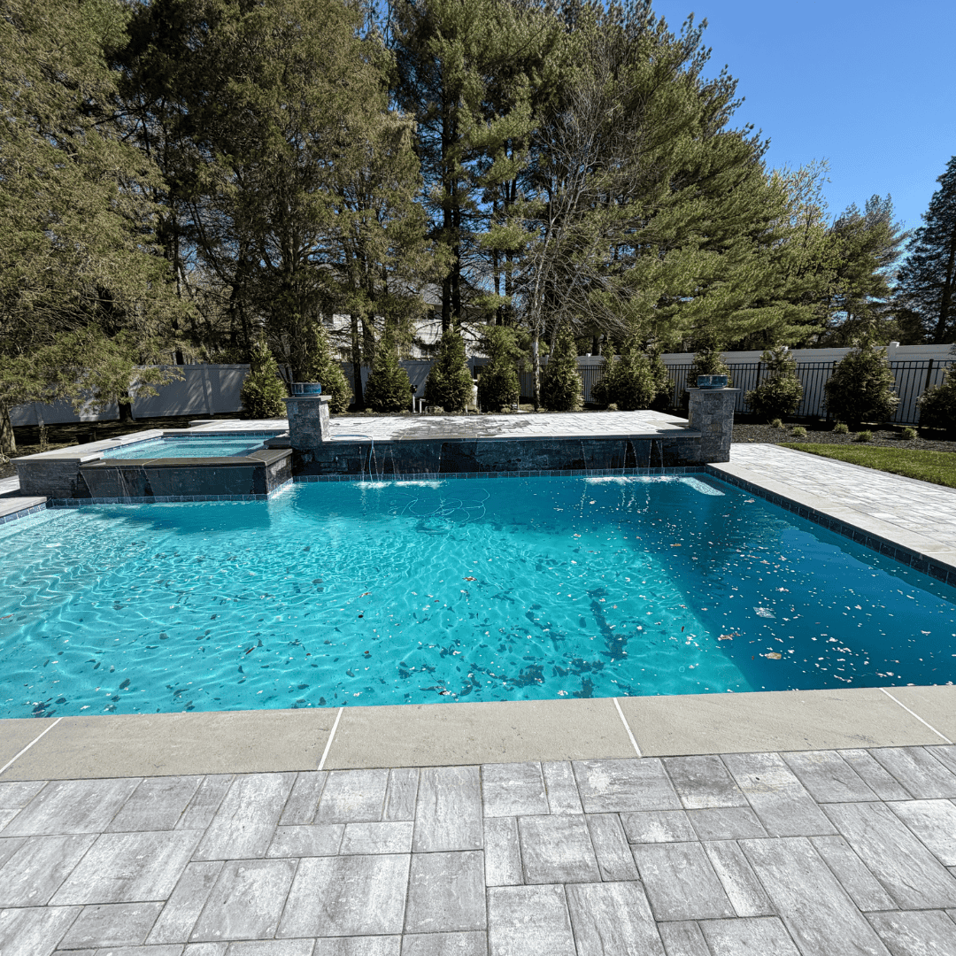 Beautiful backyard pool with waterfall feature and lush trees in the background.