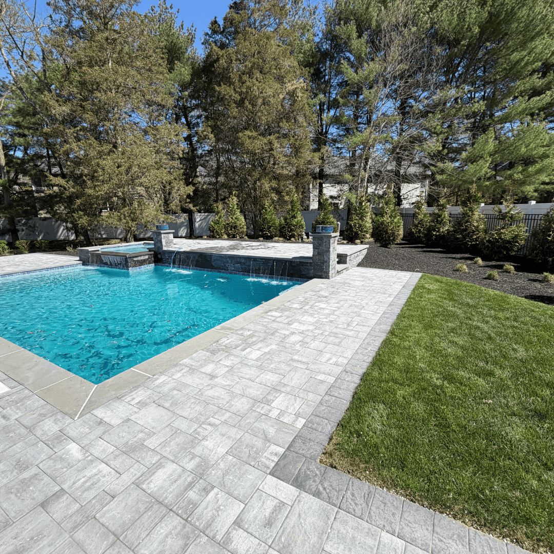 Outdoor pool area with stone patio, water feature, and surrounding greenery.