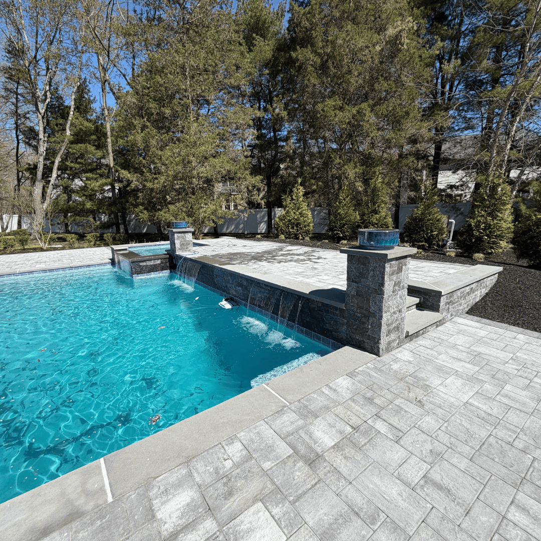 Custom backyard pool with waterfall and stone patio by C&J Outdoor Services.