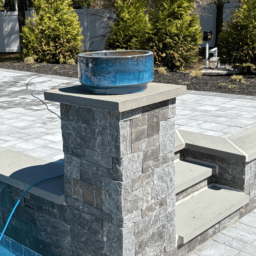 Water fountain with stone base and blue ceramic bowl in garden setting.