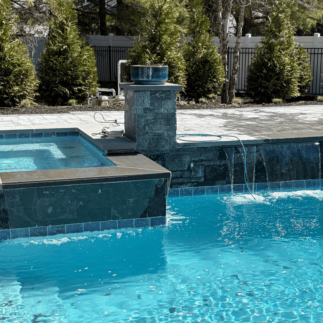 Pool water fountain with waterfall feature and spa area in backyard.