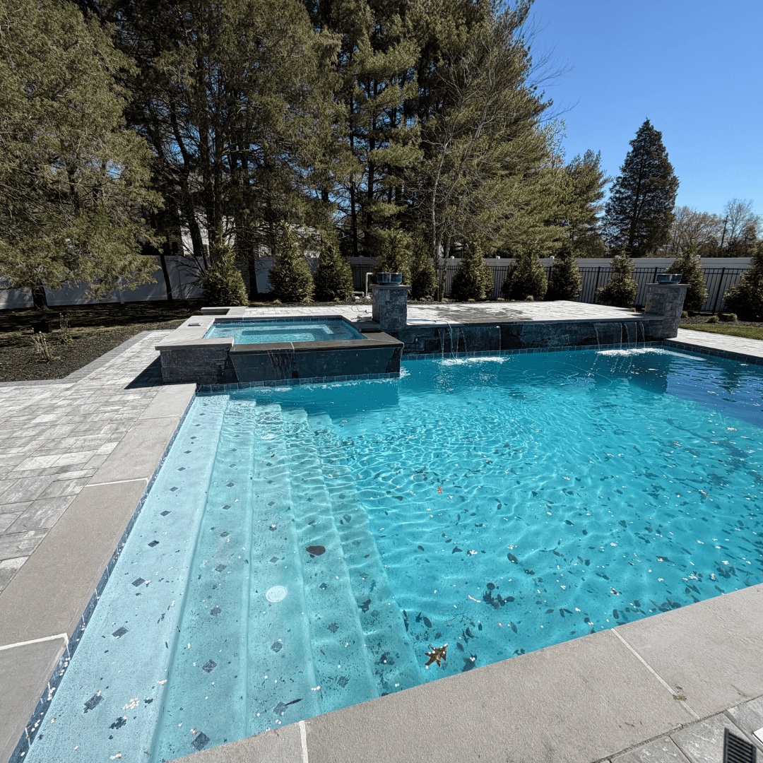 Custom backyard pool with spa and waterfall, landscaped with trees and stonework.